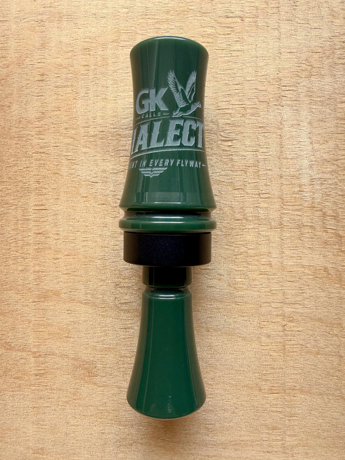 GK Calls The Dialect duck call in Hunter Green, lying on a wood board