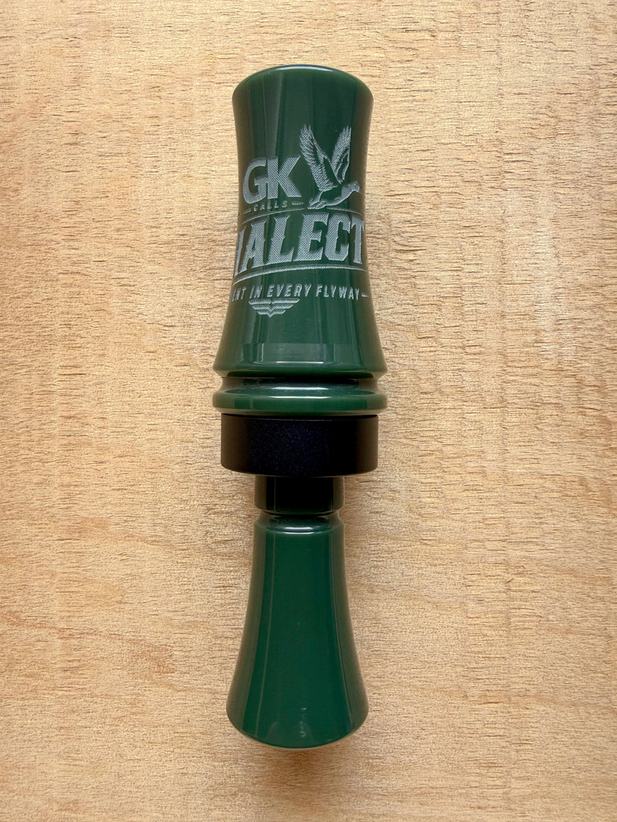 GK Calls The Dialect duck call in Hunter Green, lying on a wood board