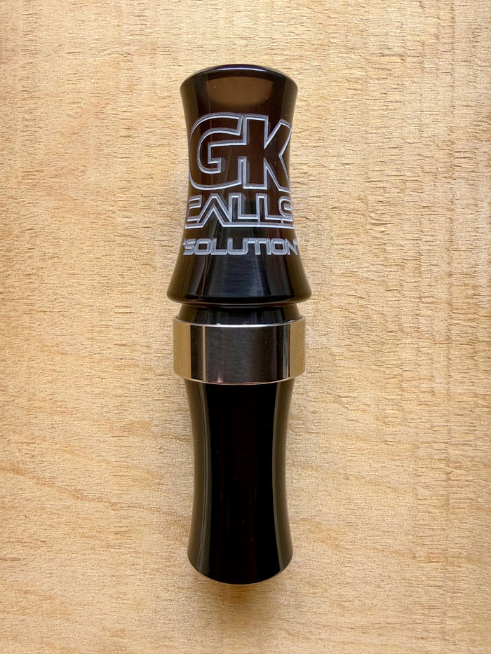 GK Calls Solution goose call in black with a metal band, lying on a wood board