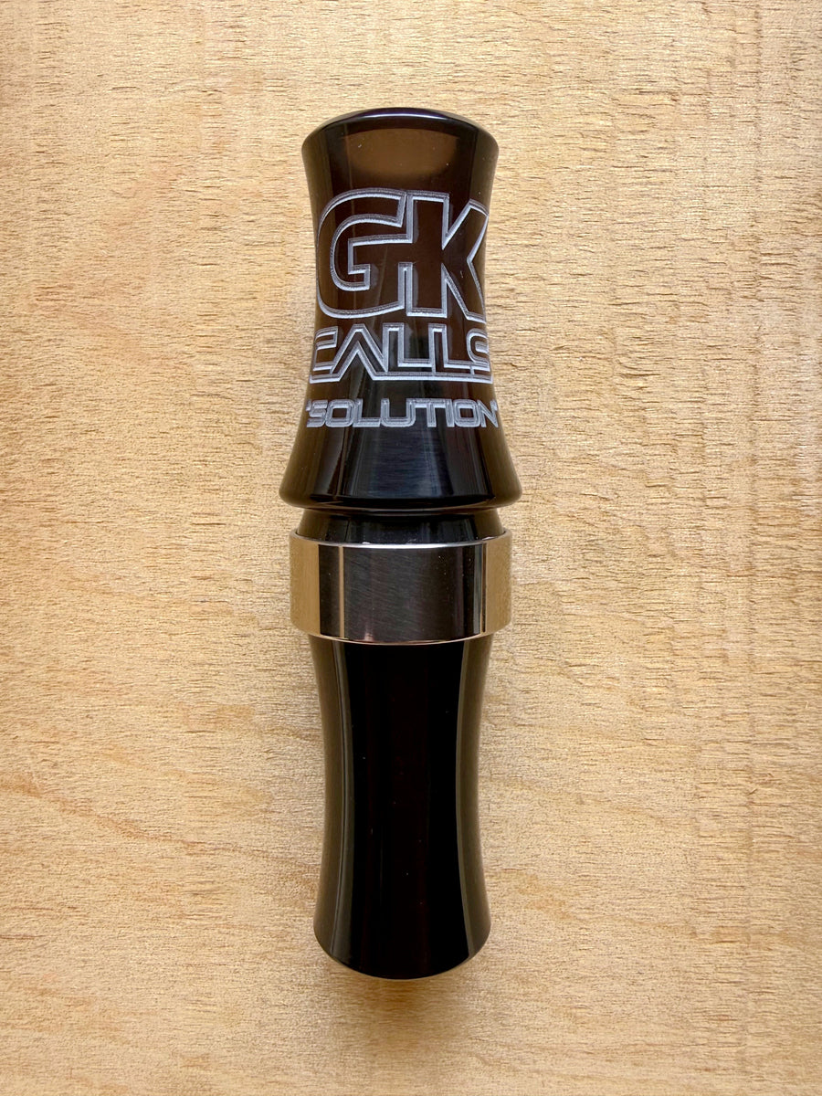 GK Calls Solution goose call in black with a metal band, lying on a wood board