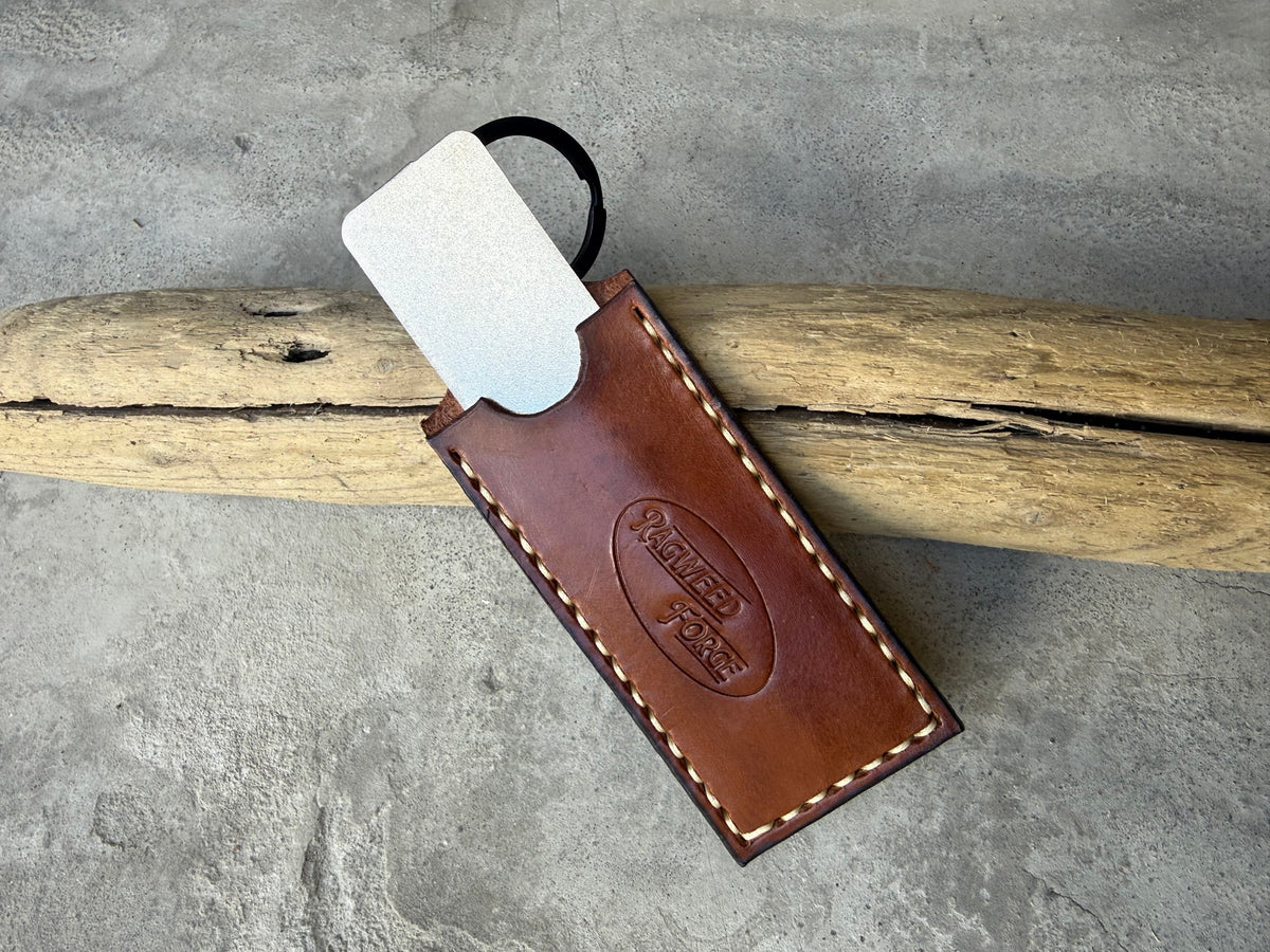 Diamond sharpening plate sliding out of a brown leather sleeve, on driftwood