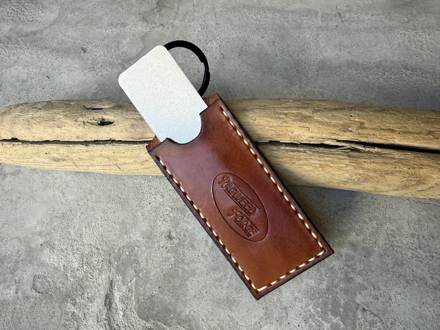 Diamond sharpening plate sliding out of a brown leather sleeve, on driftwood