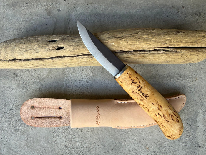 Roselli Carpenter Knife R110 with slim curly birch handle and leather sheath, resting on driftwood