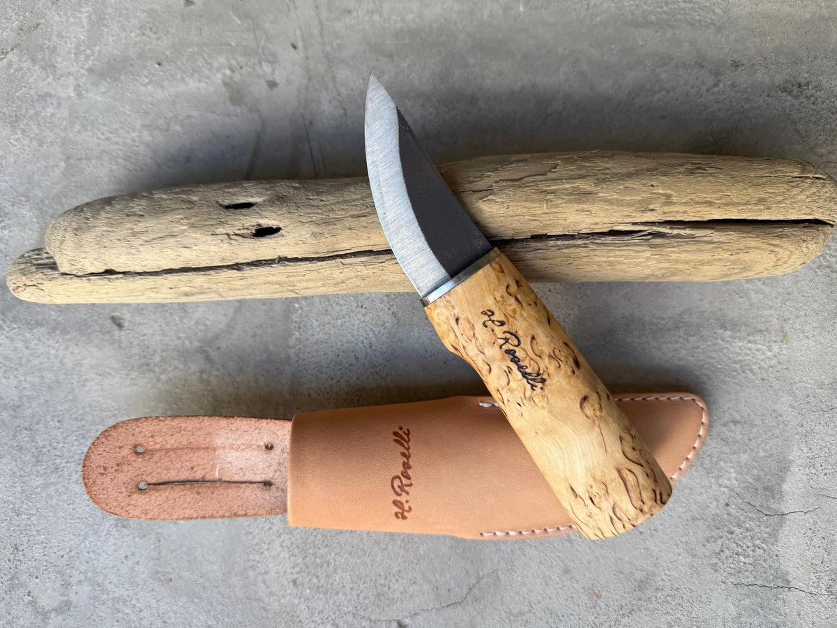 Roselli Grandfather Knife R120 with curly birch handle and leather sheath, resting on driftwood