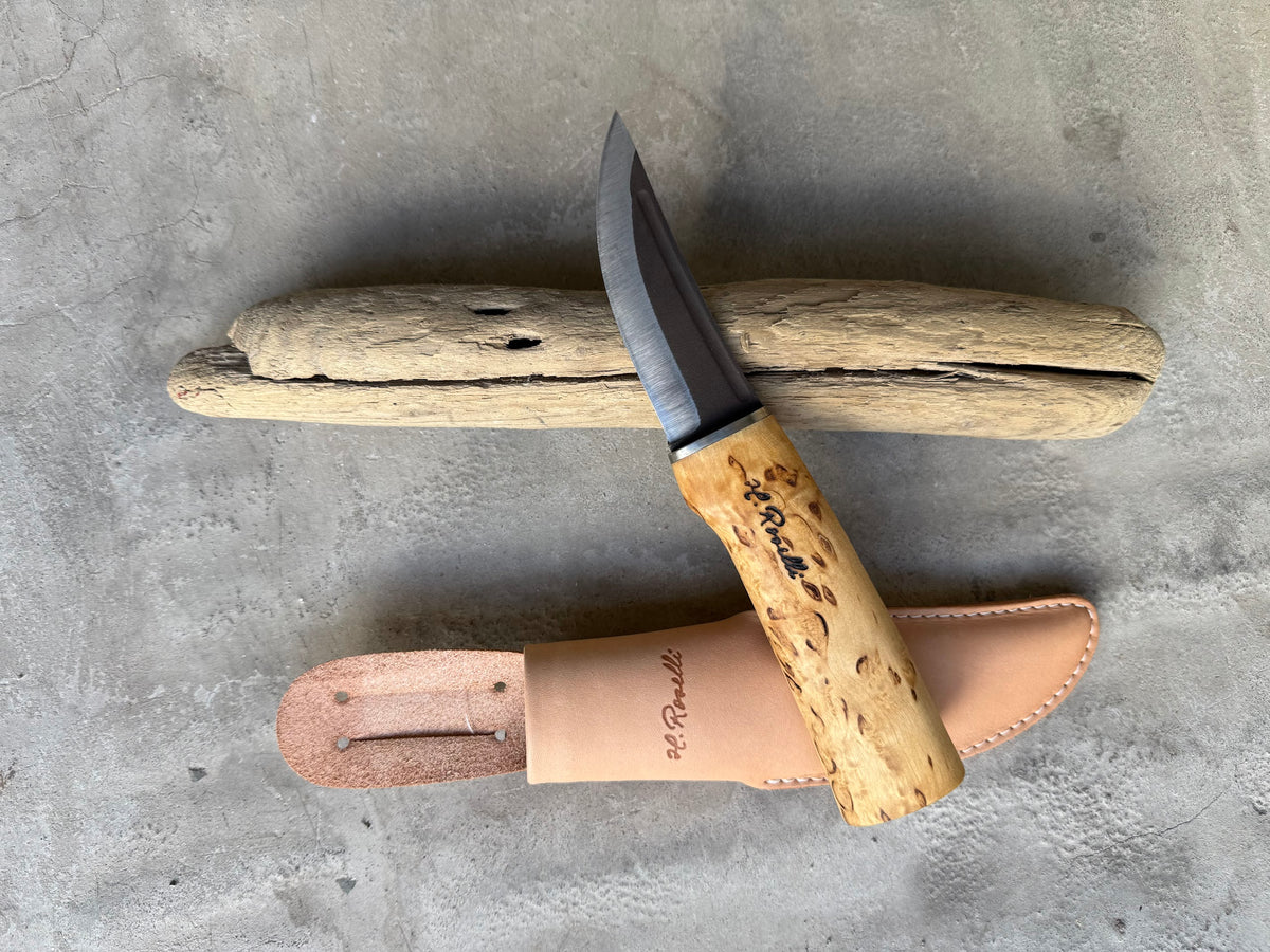 Roselli Hunting Knife R100 with curly birch handle and leather sheath, resting on driftwood